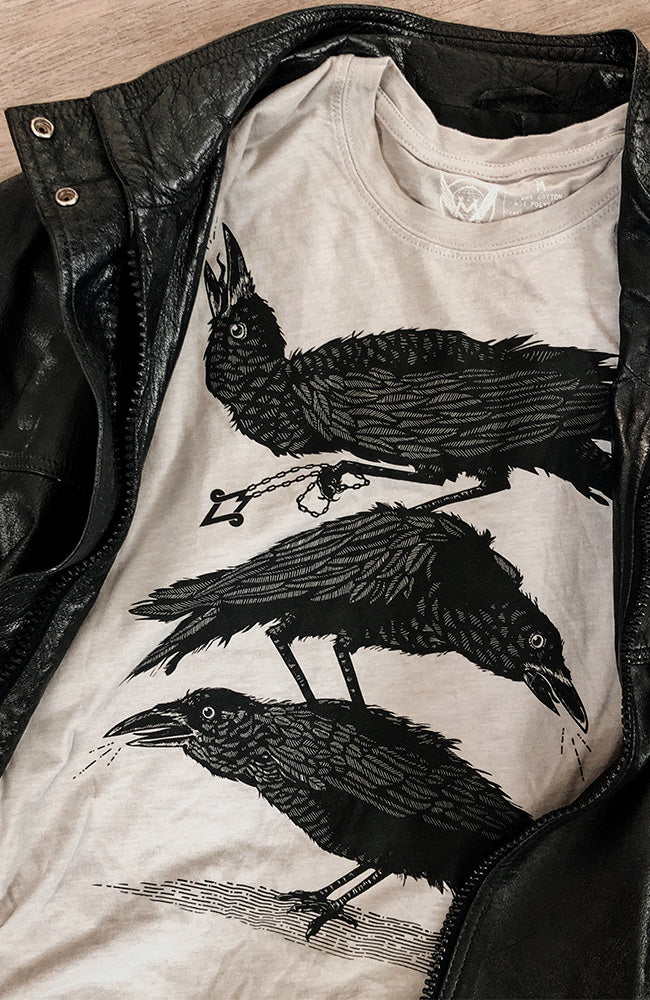 A black t-shirt with a graphic print of three crows perched in a whimsical arrangement, displayed under a black leather jacket.